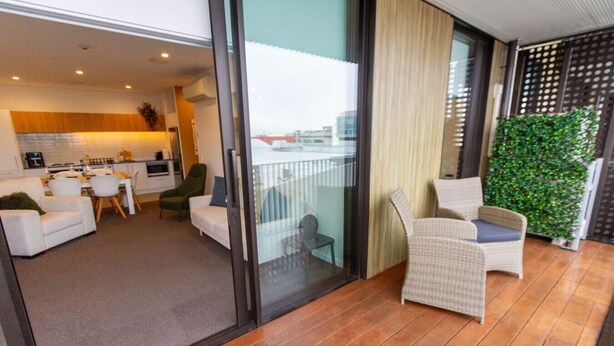 A modern living area with a sofa, chairs, a dining table, and a kitchen in the background.