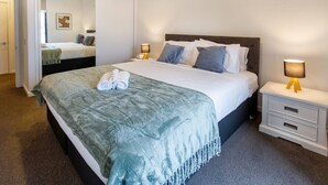 A neatly made bed with a blue blanket, two bedside lamps, and a mirror in a hotel room.