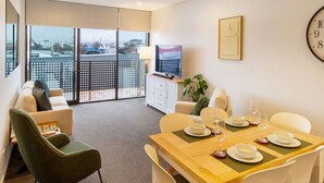 A modern living room with a dining area, large windows, a TV, and a clock on the wall.