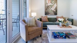 A living room with a green sofa, a beige armchair, and a coffee table with books and a clock.