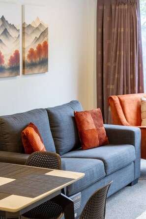 A modern living room with a grey sofa, orange pillows, a wooden coffee table, and a wicker chair. - 3bed with Garage Minutes from the Action and Sleeps 8 (Christchurch)