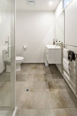 A modern bathroom with a glass shower enclosure, a white toilet, a vanity with a mirror, and a towel rack. - 3bed with Garage Minutes from the Action and Sleeps 8 (Christchurch)