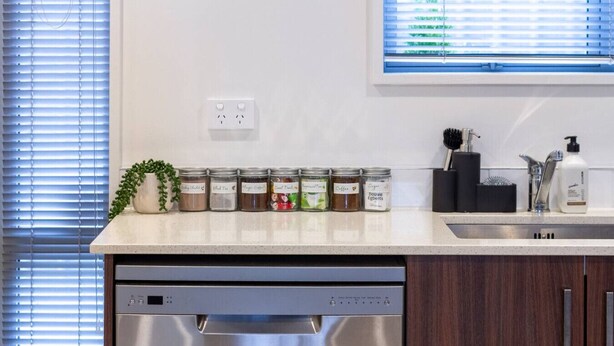 A kitchen with a dishwasher, a countertop with jars of spices, a sink, and a window with blinds. - 3bed with Garage Minutes from the Action and Sleeps 8 (Christchurch)