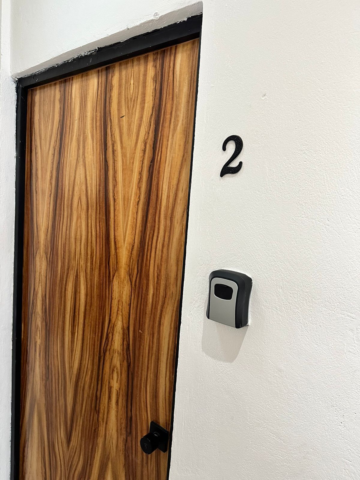 Una porta de fusta amb marc negre i el número "2" al mur de costat.