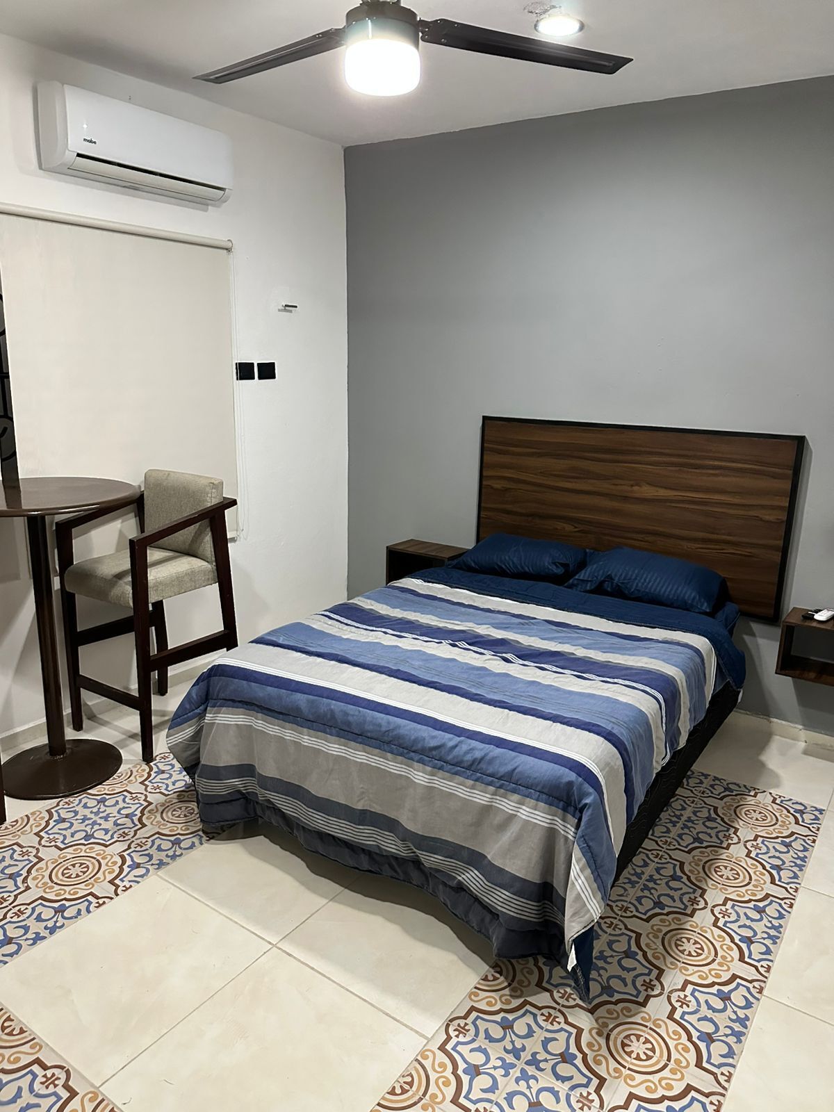 A bedroom with a bed, a chair, a nightstand, an air conditioner, and a ceiling fan.