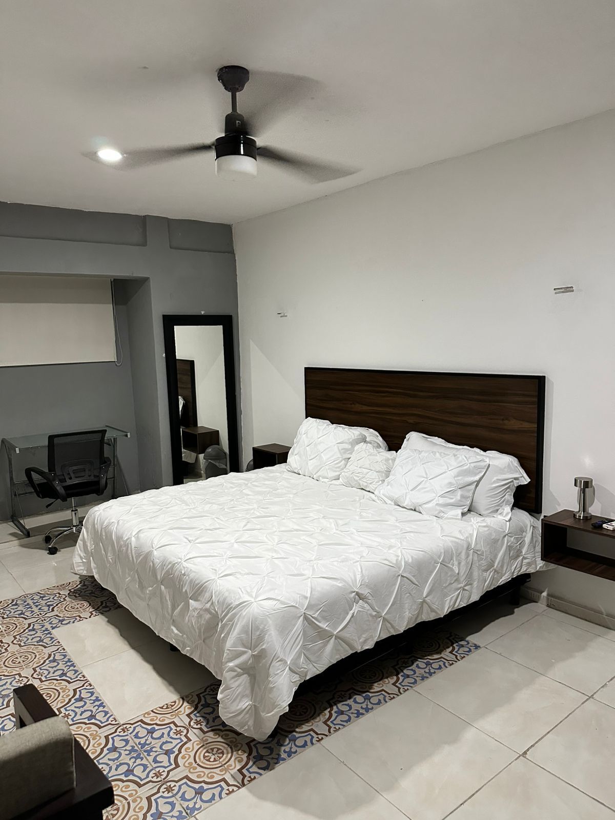 A modern bedroom with a large bed, a ceiling fan, and a desk with a chair.