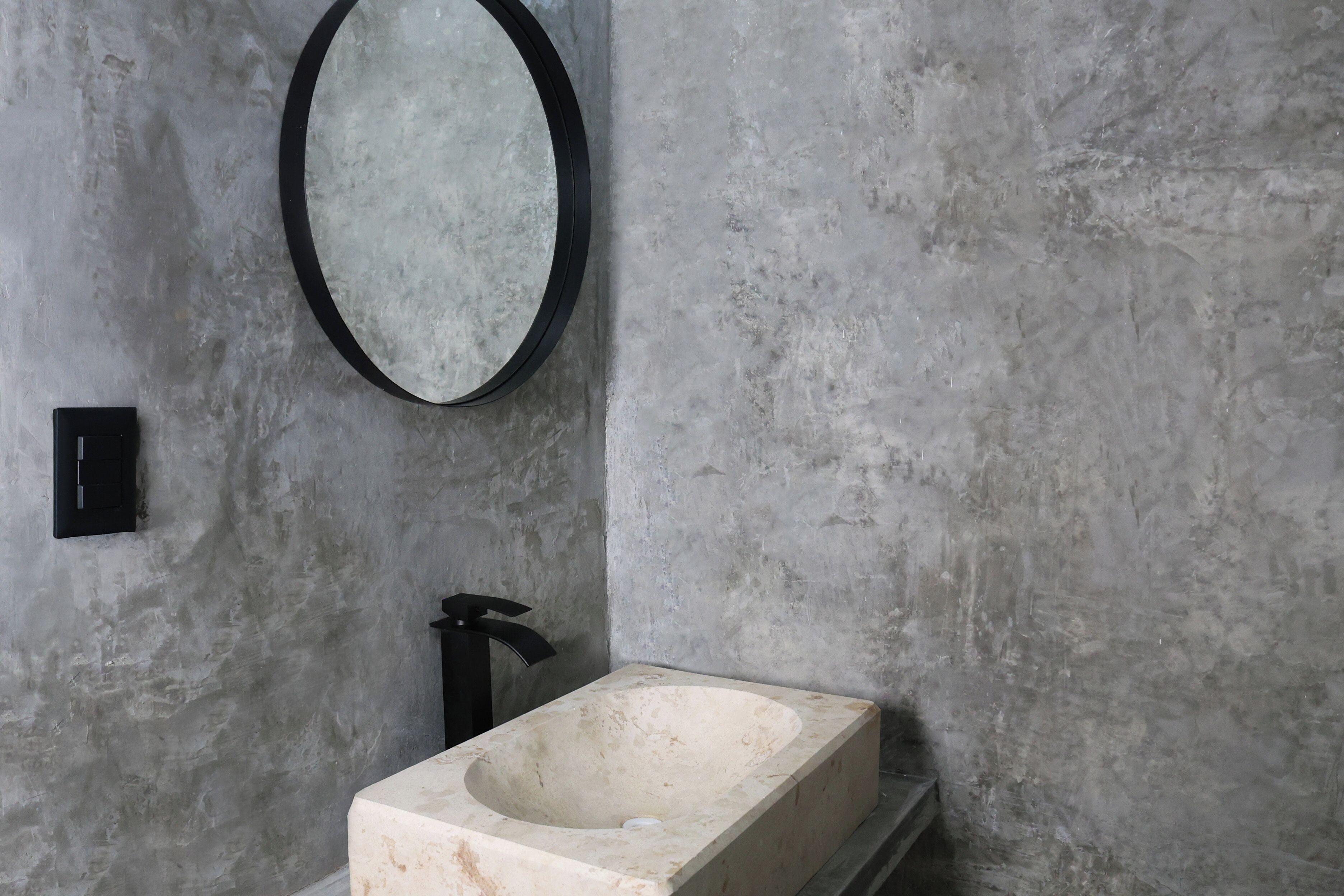 A bathroom with a rectangular sink, a round mirror, and a black faucet.