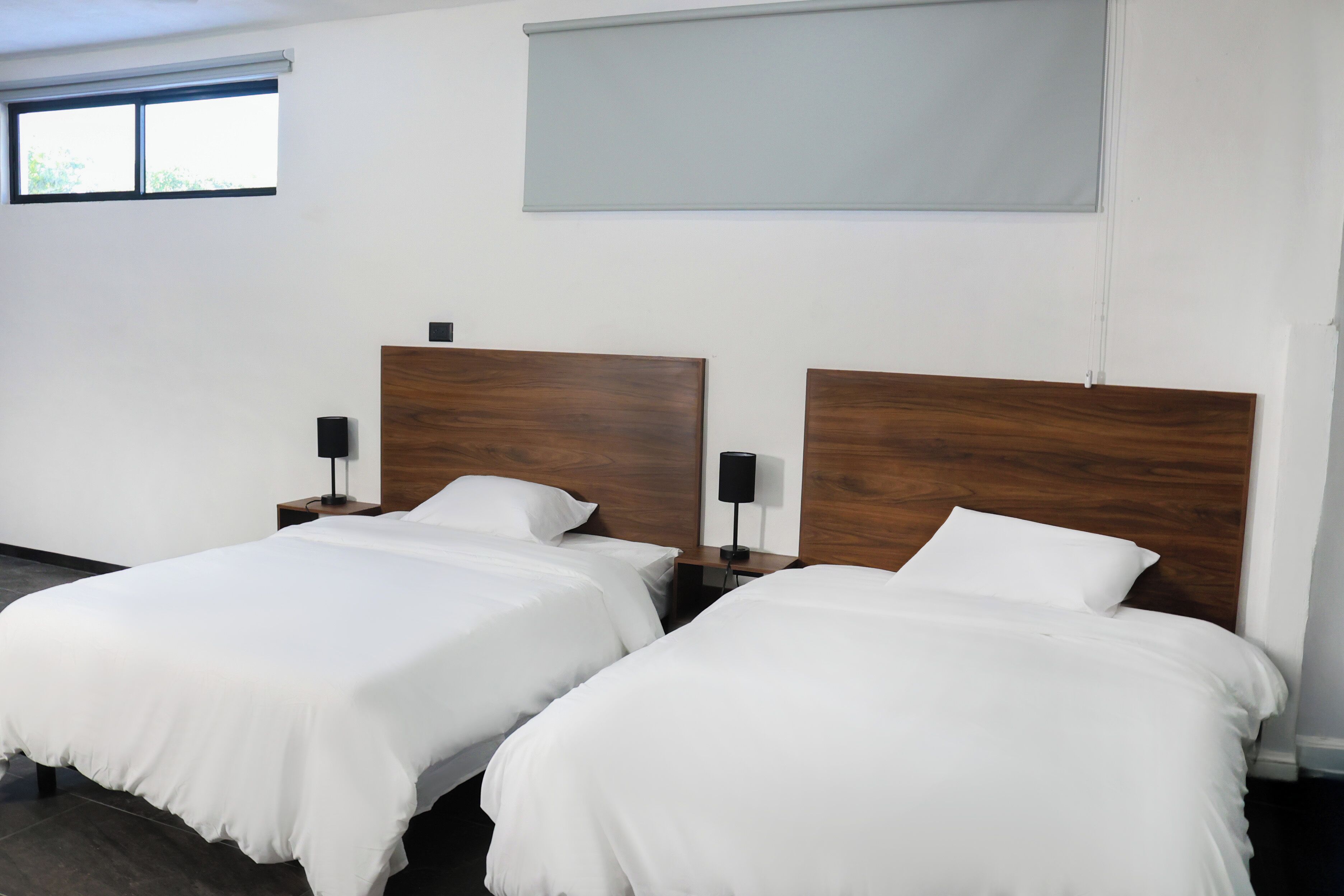 Une chambre d’hôtel avec deux lits, chacun doté d’une tête de lit en bois, de draps blancs et de lampes de chevet.