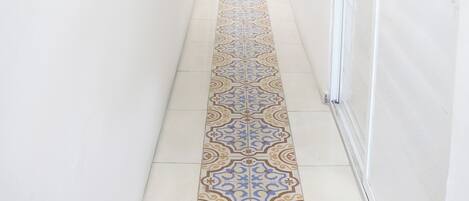 A long, narrow hallway with white walls and a patterned tile floor.