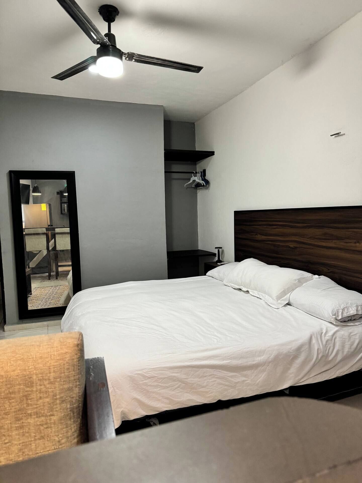 Une chambre à coucher avec un lit, un ventilateur de plafond, une table de chevet et un miroir.
