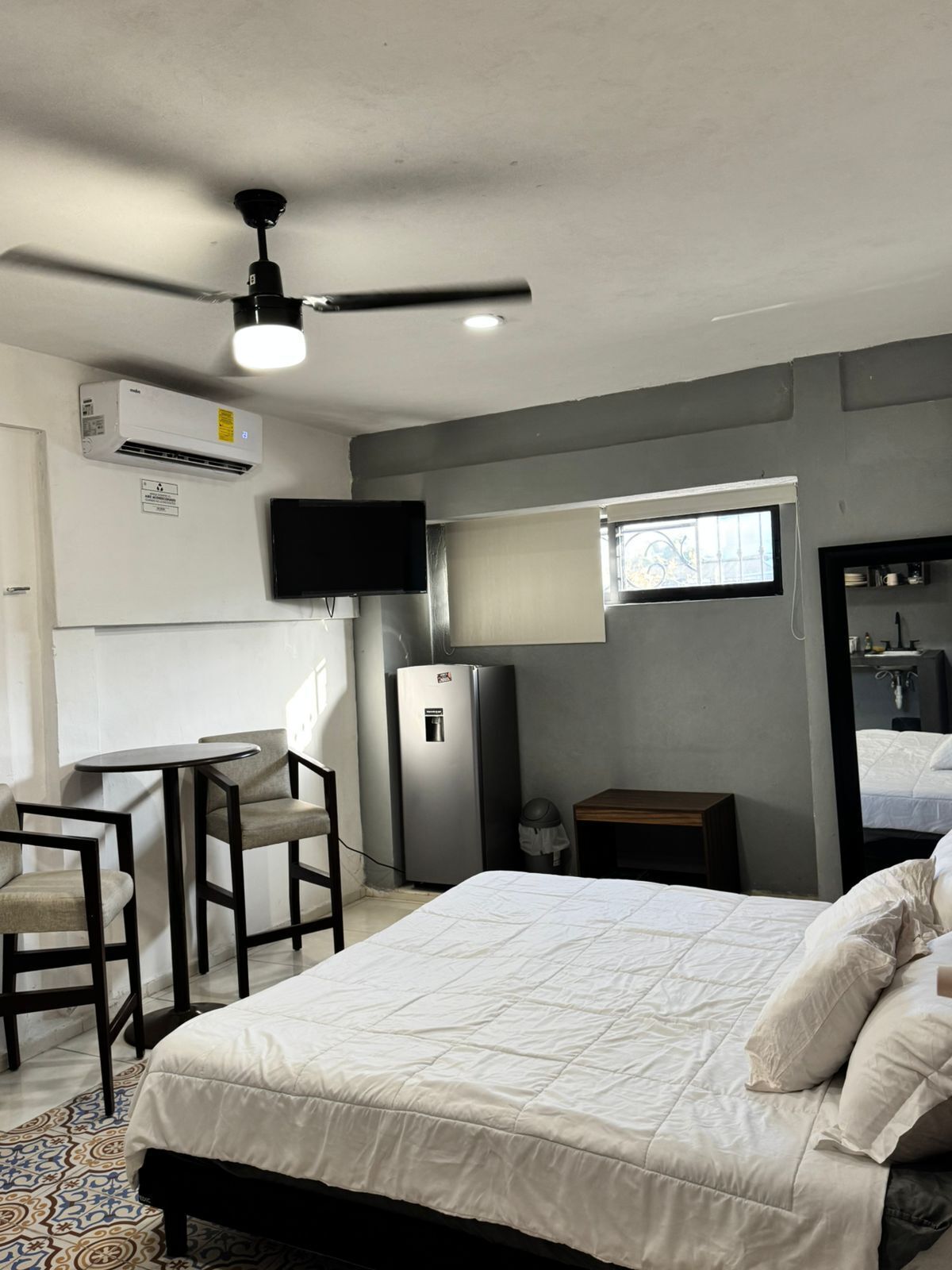 A bedroom with a bed, a desk, a chair, a television, and a ceiling fan.