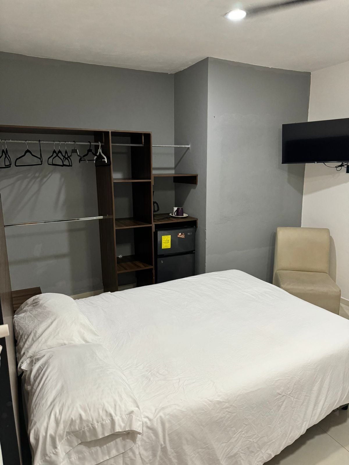 A bedroom with a bed, a wardrobe, a television, and a chair.