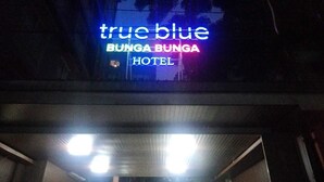 The exterior of the True Blue Bunga Bunga Hotel with a neon sign and a covered entrance. - Hotel Bunga Bunga (Jakarta)