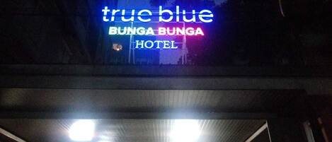 Exterior del Hotel True Blue Bunga Bunga, con un letrero de neón y una entrada cubierta.