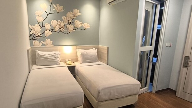 A small, neatly arranged bedroom with two single beds, a wall-mounted light fixture, and a door leading to another room. - Hotel Bunga Bunga (Jakarta)