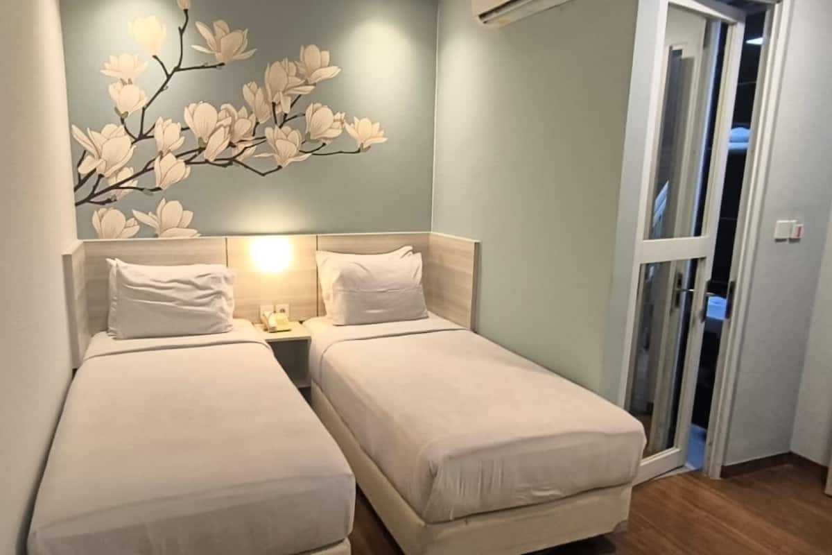Une petite chambre à coucher, bien rangée, avec deux lits simples, un luminaire fixé au mur et une porte donnant sur une autre pièce.