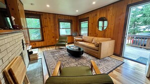 A cozy living room with a fireplace, wooden walls, a leather sofa, a coffee table, and a view of the outdoors. - McCall Me Cozy, McCall Me Cozy (Valley County)