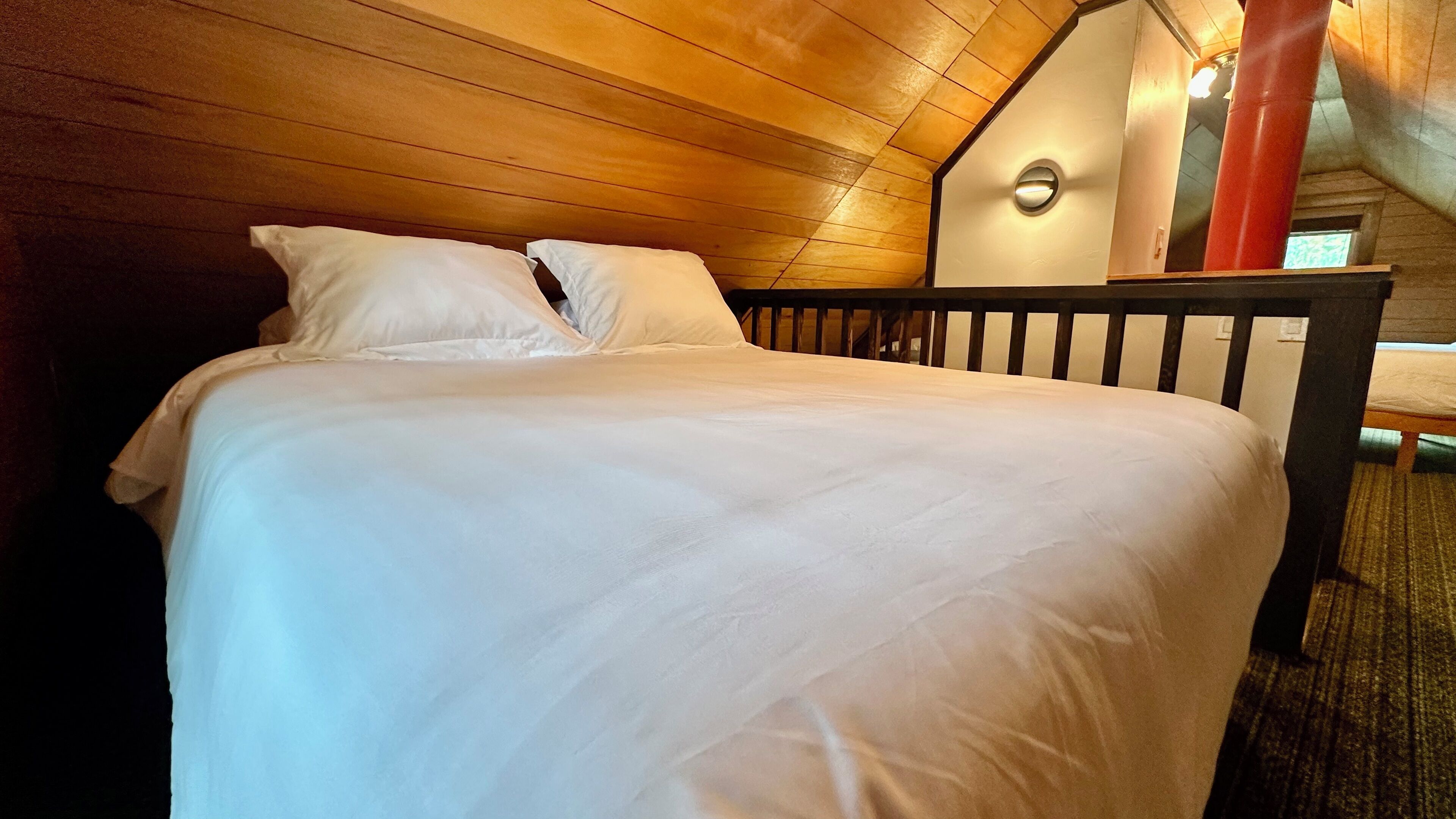 A neatly made bed with white linens in a room with wooden walls and a sloped ceiling.