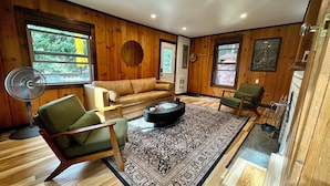 A cozy room with wooden walls, a sofa, a green armchair, a coffee table, and a fan. - McCall Me Cozy, McCall Me Cozy (Valley County)