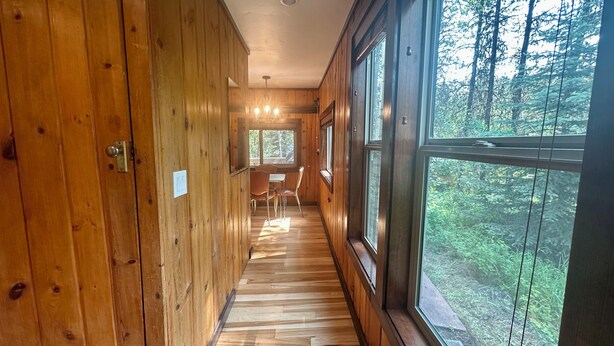 A wooden interior hallway with large windows, a dining area, and a door with a light switch. - McCall Me Cozy, McCall Me Cozy (Valley County)