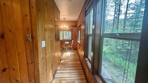 Un couloir intérieur en bois, doté de grandes fenêtres, d’un coin repas et d’une porte avec un interrupteur.