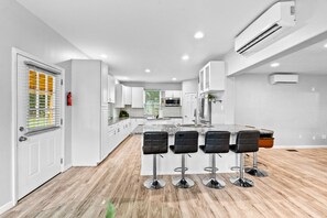 A modern kitchen with white cabinets, a central island with bar stools, and a herringbone-patterned backsplash. - Family Getaway 4BR w/ Game Loft & Fire Pit (Lilburn)