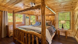Een slaapkamer in een blokhut met een hemelbed, houten wanden en een raam met jaloezieën.