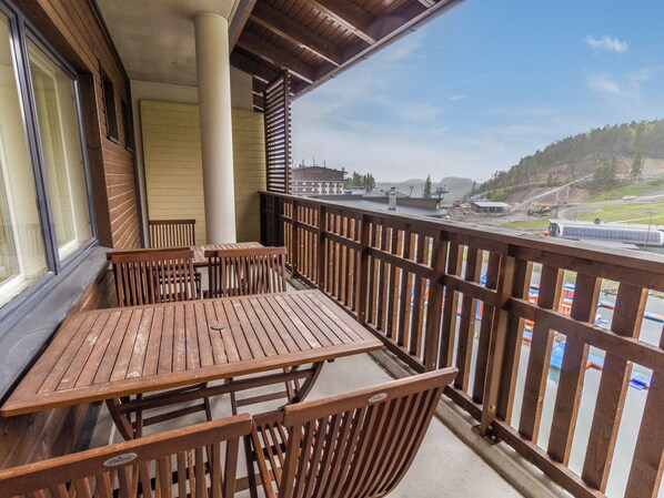 A balcony with wooden furniture, a view of a building, and a clear sky.