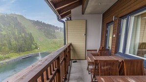 Un balcon doté de balustrades en bois, offrant une vue sur une rivière et un paysage montagneux.