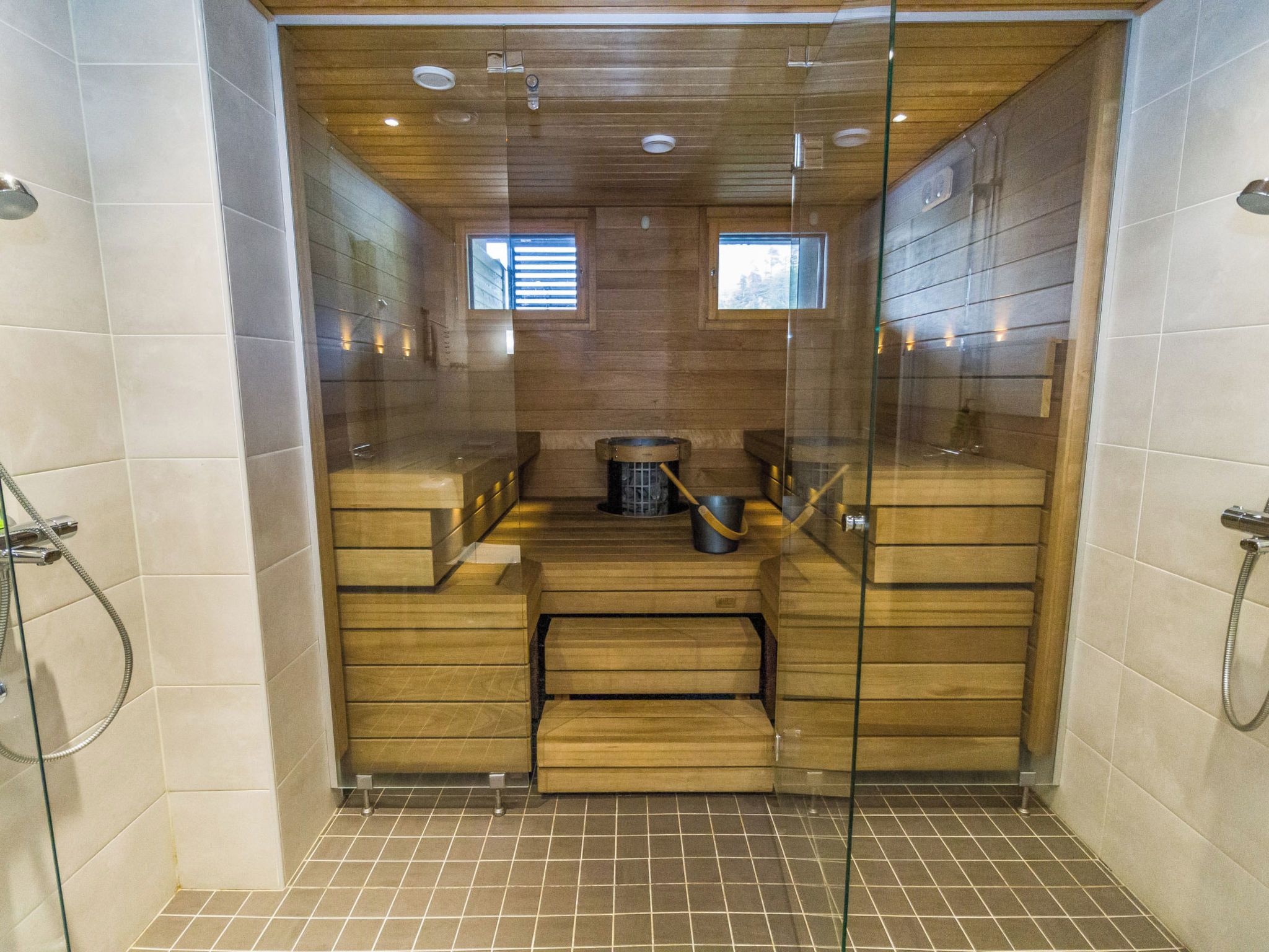 A sauna with wooden benches, a stove, and a glass partition.