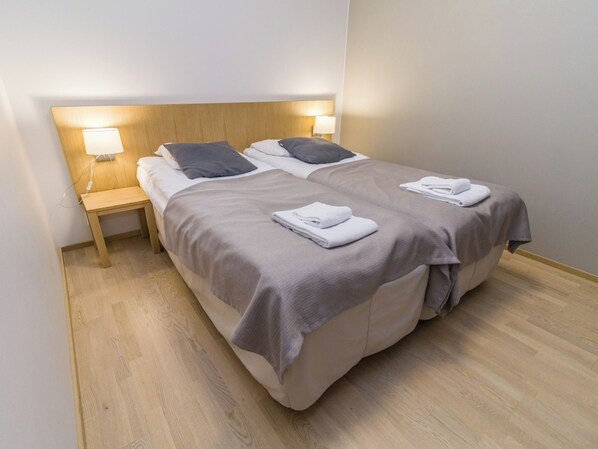 Cama doble con cabecera de madera, dos lámparas de noche y una toalla doblada sobre la cama.