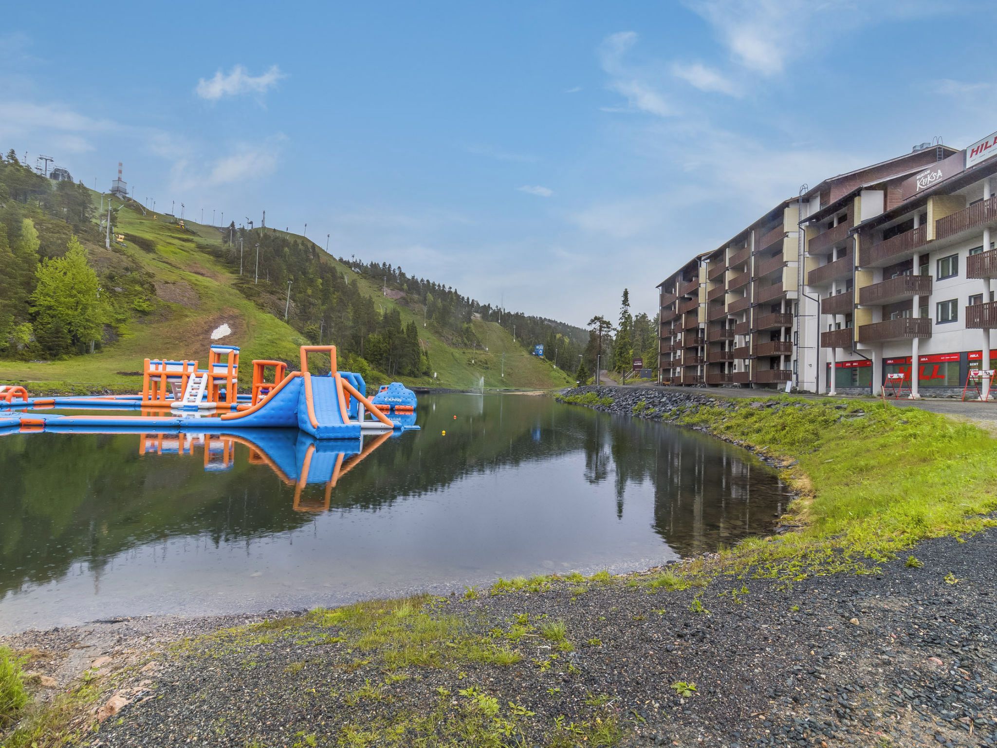 A calm river with a playground and a multi-story building with balconies.
