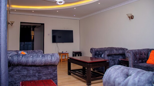 A living room with tufted sofas, a wooden coffee table, a flat-screen TV mounted on the wall, and recessed lighting. - Homely, Lovely and spacious 3-bedroom bed & breakfast in Bungoma (Bungoma)