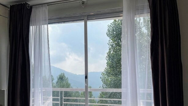 Ein Zimmer mit einer großen Schiebeglasdoor, die auf einen Balkon führt. Der Balkon hat ein Metallgeländer und einen gemusterten Boden.