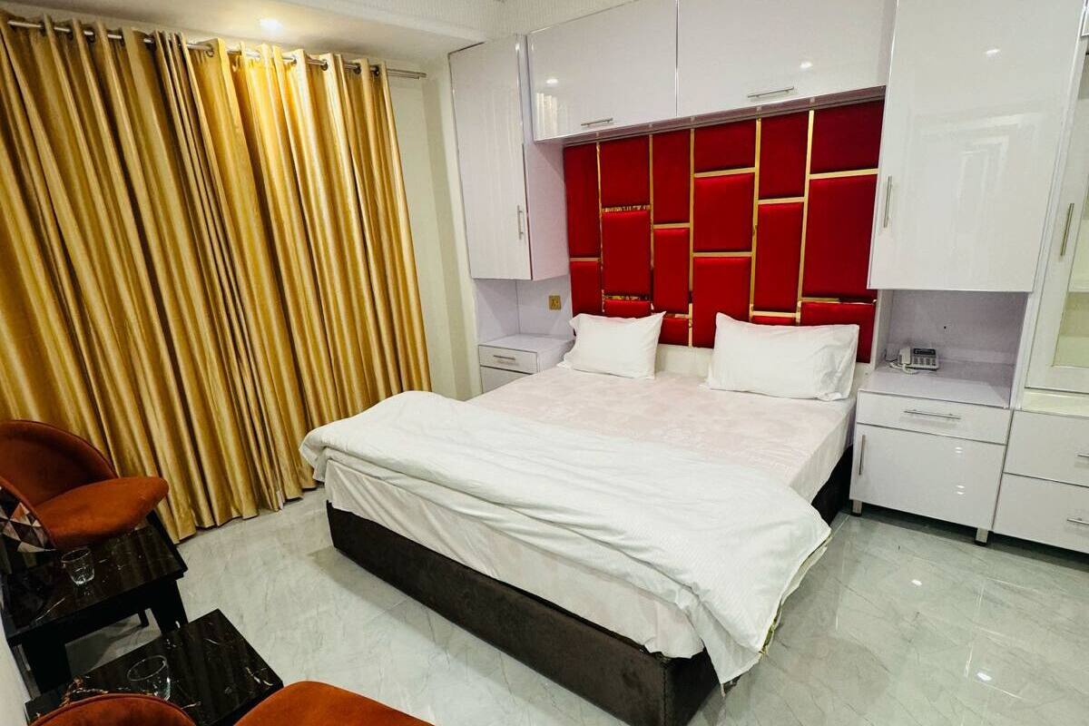 A modern bedroom with a large bed, a chest of drawers, and a seating area with a patterned chair.