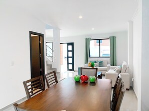 Un comedor con una mesa y sillas de madera, un sofá y una ventana con cortinas.