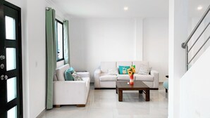 Una sala de estar moderna con un sofá blanco, una mesa de centro con un florero y una escalera a la derecha.