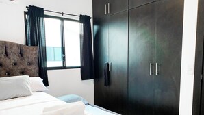 Un dormitorio con cama, armario y ventana con cortinas.