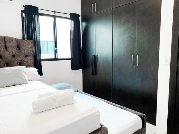 Un dormitorio con cama, armario y ventana con cortinas.