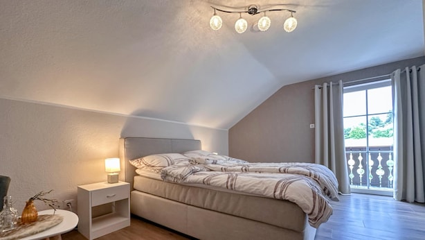 Une chambre à coucher comprenant un lit, une table de chevet, une lampe et une fenêtre donnant sur l’extérieur.