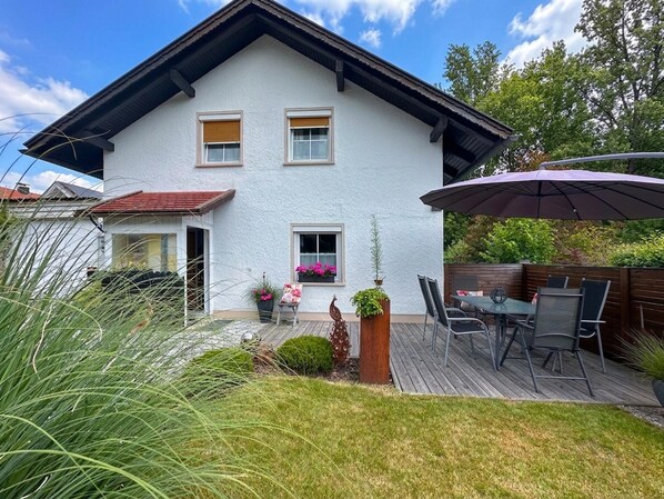 A two-story house with a deck, a patio with chairs, and a large umbrella. - Holiday home with terrace in the Bavarian Forest (Waldkirchen)