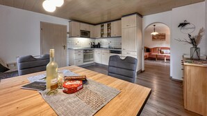Une cuisine moderne avec des meubles en bois, une table à manger avec une bouteille et des en-cas, et un coin salon avec un canapé et des objets décoratifs.
