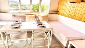 A dining area with a white table set for four, a wooden bench, and a view of a mountainous landscape through large windows. - Welooveyou Wildlife Zen (La Lajita)