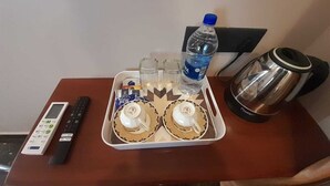 Una bandeja con dos tazas de café, una botella de agua, un control remoto y una tetera sobre una mesa de madera.