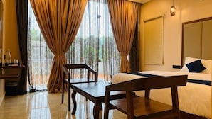 Habitación de hotel con cama, escritorio y silla. Hay cortinas en las ventanas, y una lámpara en la pared.
