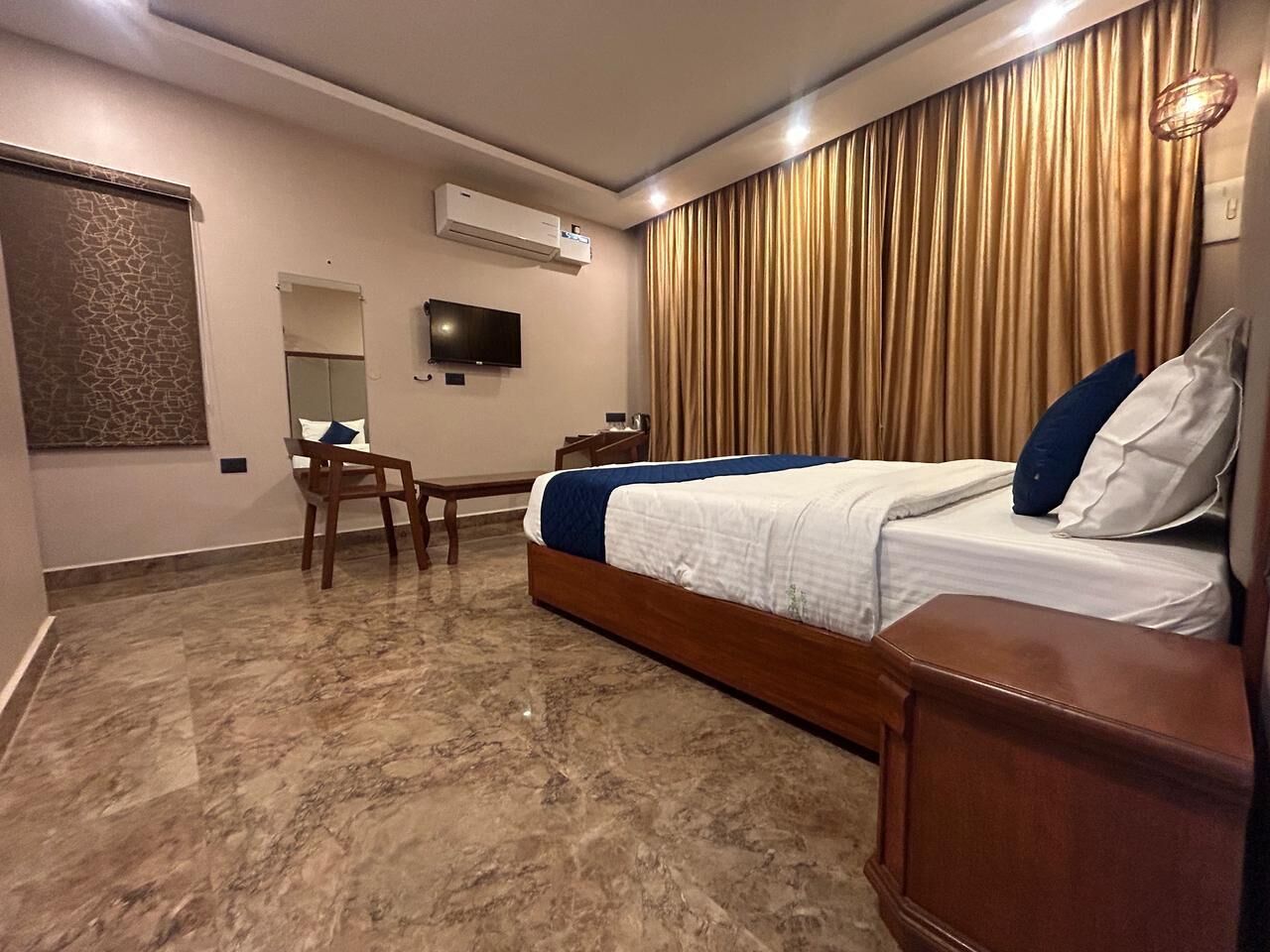 Ein Hotelzimmer mit einem Bett, einem Schreibtisch, einem Sessel, einem Fernseher und einem großen Fenster mit Vorhängen.