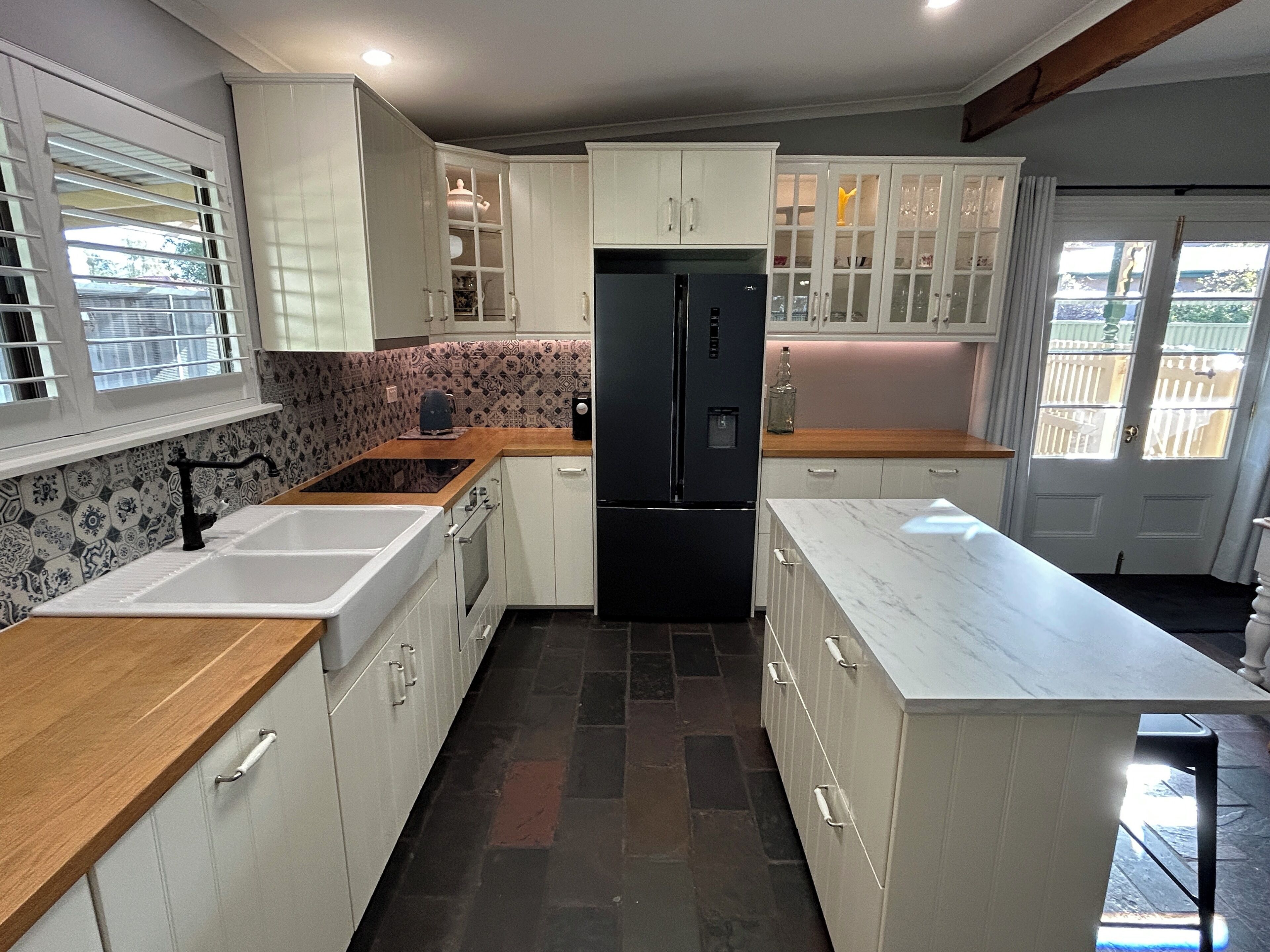 A modern kitchen with white cabinetry, a black refrigerator, and a wooden countertop.