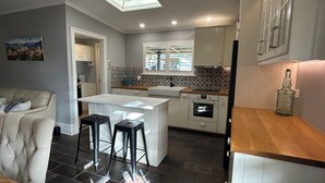 A compact kitchen with a central island, a dining area with a sofa, and a view of the cityscape through the window. - "GraciaDeDios" Beautifully renovated 1910 Cottage (Mount Barker)