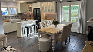 A modern kitchen with white cabinets, a black refrigerator, and a dining area with a wooden table and chairs. - "GraciaDeDios" Beautifully renovated 1910 Cottage (Mount Barker)