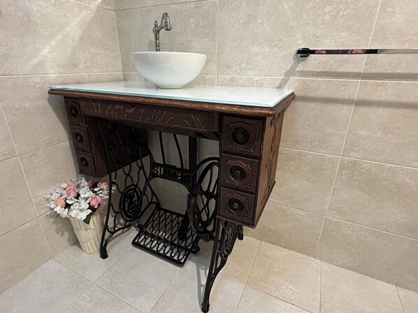 A bathroom with a white sink on a wooden vanity, a towel rack, and a decorative vase with flowers.